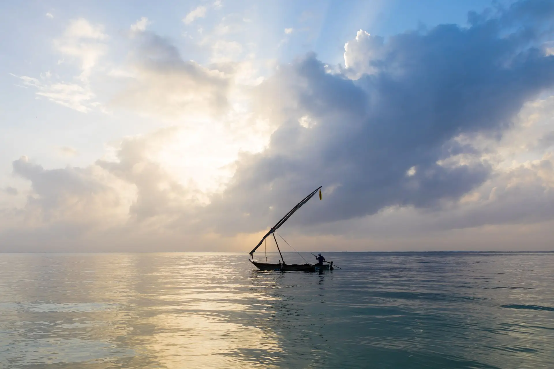 A fisherman sails a traditional dhow on calm coastal waters at sunrise